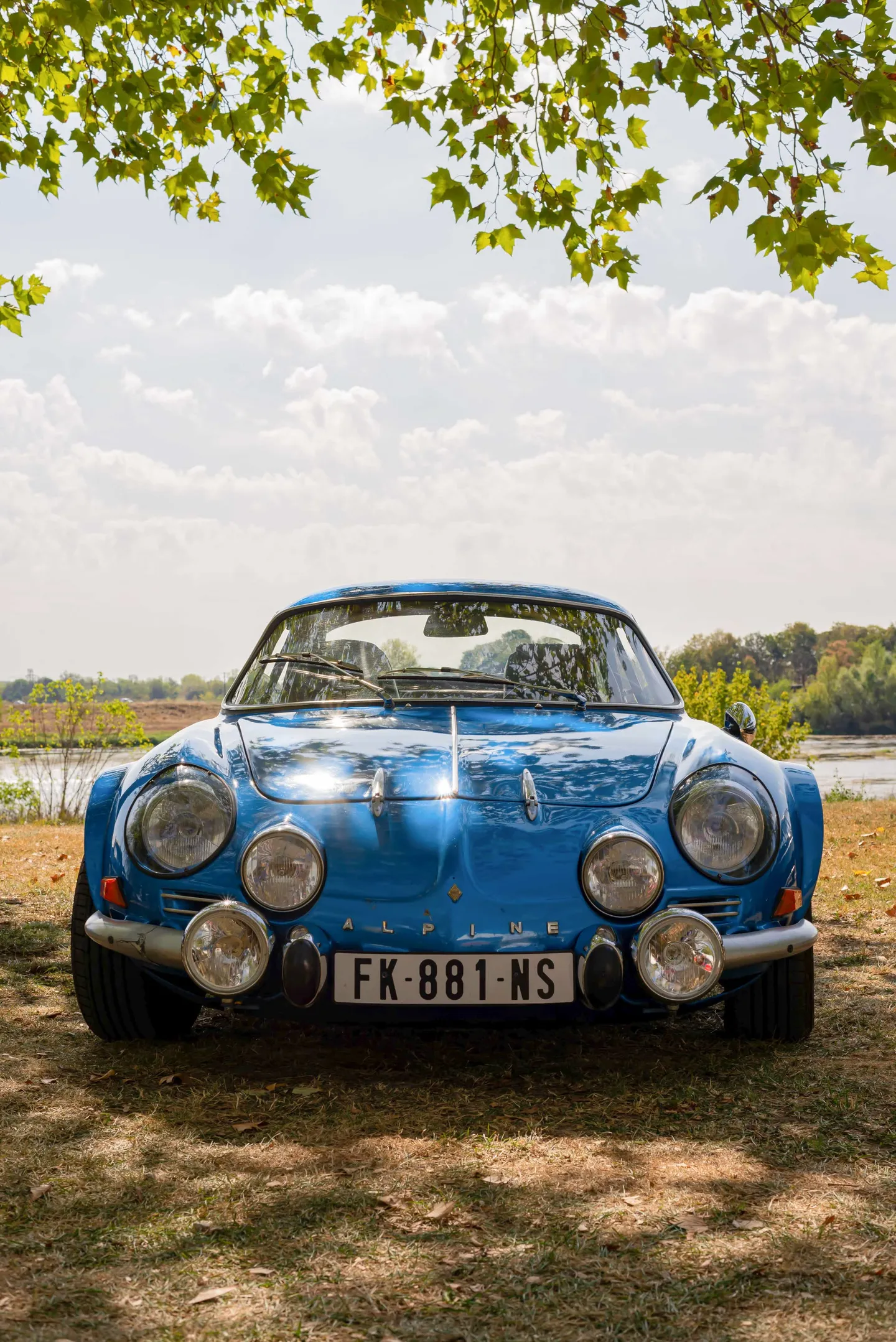 Voiture ancienne bleue garée sous les arbres